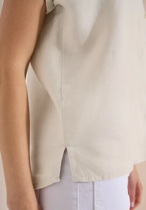 Seitliches Detail eines beige Tops mit Schlitz, getragen zu weißen Hosen.