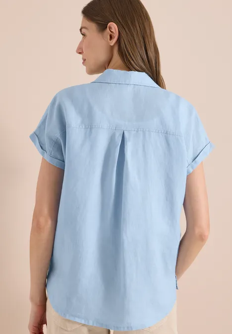 Vrouw van achteren in lichtblauw, losvallend jeansblouse met korte mouwen.