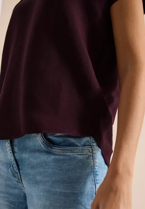 Person trägt lila Oberteil und blaue Jeans, Sicht von Taille bis Hüfte mit sichtbarem Arm