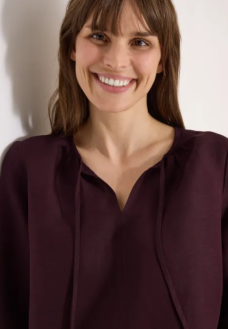 Vrouw in bordeaux top, schouderbeeld met wazig gezicht, los haar, lichte achtergrond.