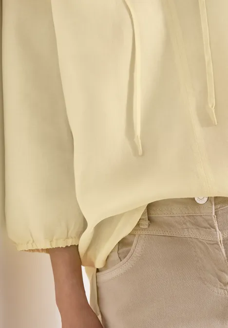 Close-up van persoon in lichtgele trui met trekkoord en beige broek.