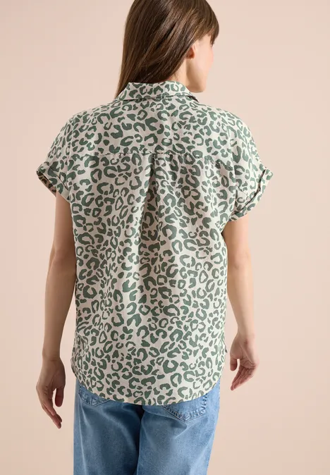 Vrouw van achteren in een groen-wit luipaardprint blouse met korte mouwen en een spijkerbroek.