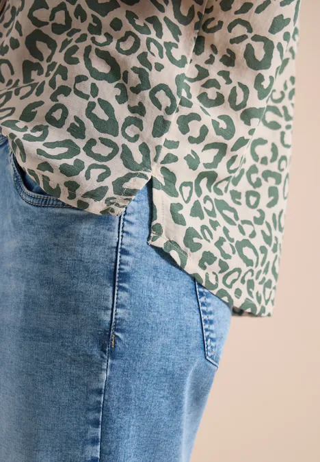 Close-up van een groene luipaardprint-blouse en een blauwe spijkerbroek.
