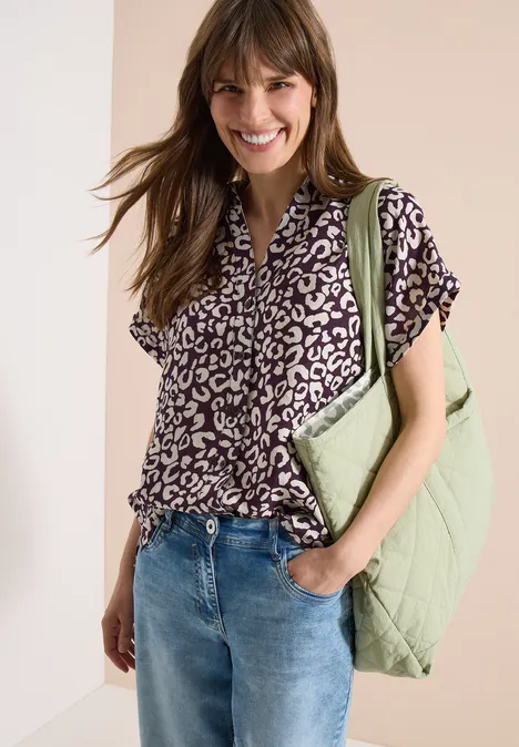 Vrouw draagt blouse met korte mouwen in zwart-wit luipaardprint, high-waist jeans en een lichtgroene, gewatteerde schoudertas.