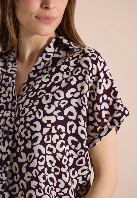 Vrouw in paars-wit kort mouwen overhemd met luipaardprint voor een neutrale achtergrond.