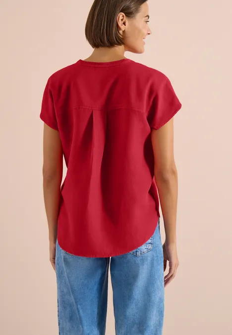 Rugaanzicht van persoon in rood shirt met korte mouwen en blauwe spijkerbroek voor beige achtergrond.