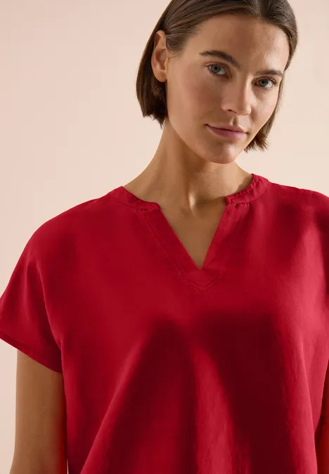 Vrouw met rode blouse en V-hals tegen neutrale achtergrond