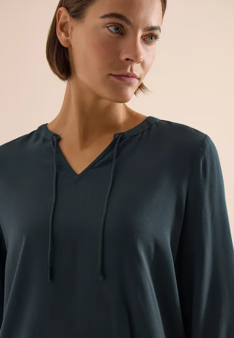 Donkergroen langärmelig shirt met V-hals en koordjes bij de nek.