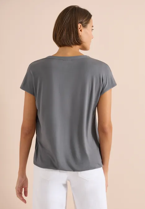 Achteraanzicht van een persoon in een grijs t-shirt en witte broek tegen een neutrale achtergrond.