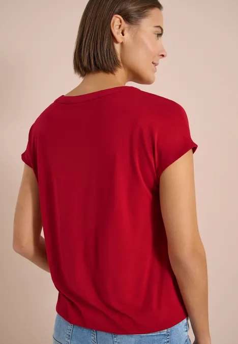 Vrouw van achteren met rood T-shirt tegen een lichte achtergrond