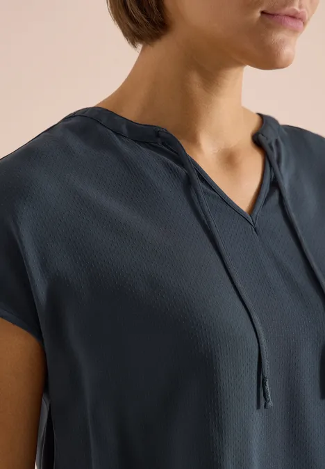 Vrouw in donkerblau kort mouw blouse met V-hals en fijne koordjes, close-up van het bovenlichaam