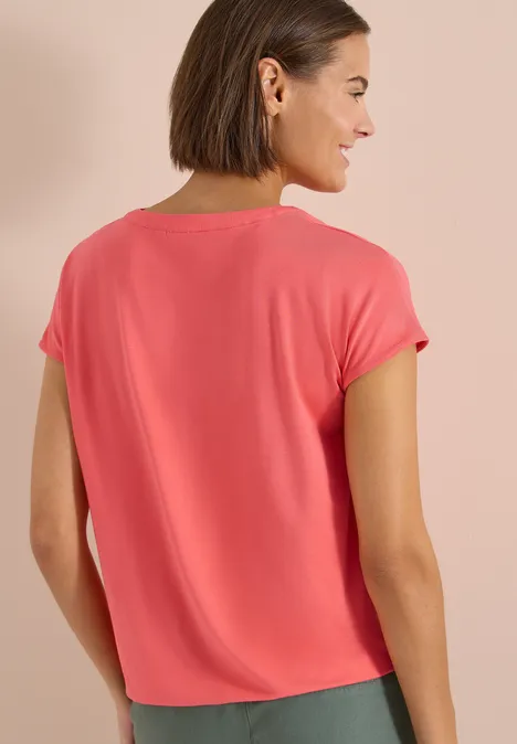 Vrouw van achteren in een koraalrood t-shirt met korte mouwen voor een neutrale achtergrond.
