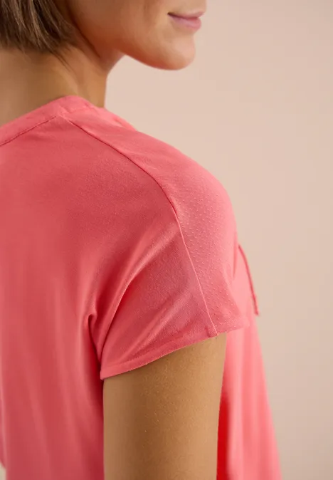 Close-up van een vrouw in een koraalkleurig T-shirt, focus op schouder en mouwnaad.