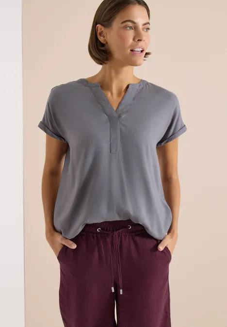 Blouse met korte mouwen en gespleten hals graphite light grey Vrouw in grijsblauw V-hals shirt en bordeauxrode broek met trekkoord, handen in de zakken.
