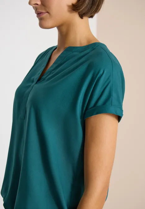Blouse met korte mouwen en gespleten hals jungle green Vrouw in profiel draagt een groenblauw shirt met korte mouwen, losse pasvorm en V-hals.