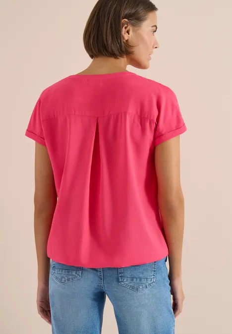 Blouse met korte mouwen en gespleten hals geranium red Vrouw van achteren in een felroze blouse met korte mouwen en spijkerbroek voor neutrale achtergrond.
