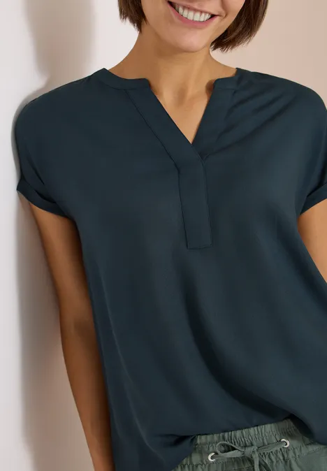 Kurzarm Bluse mit Split Neck deep petrol blue Eine lachende Frau in einer dunkelblauen Bluse vor hellem Hintergrund.