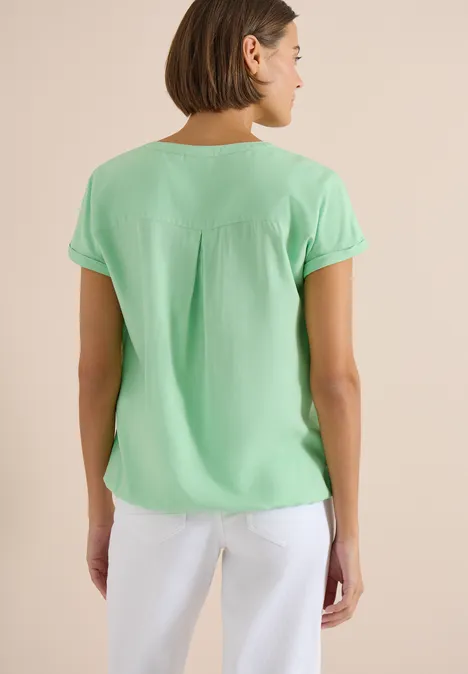 Blouse met korte mouwen en gespleten hals juicy lime Vrouw van achteren in mintgroene blouse met korte mouwen en witte broek.