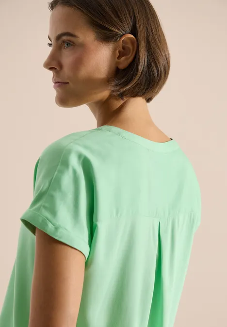 Blouse met korte mouwen en gespleten hals juicy lime Achteraanzicht van een persoon in een losse groene blouse met korte mouwen.