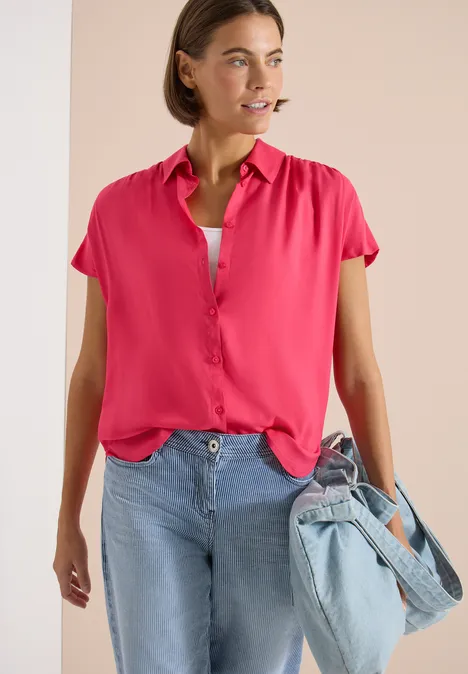 Vrouw in roze blouse, lichte spijkerbroek en spijkertas.