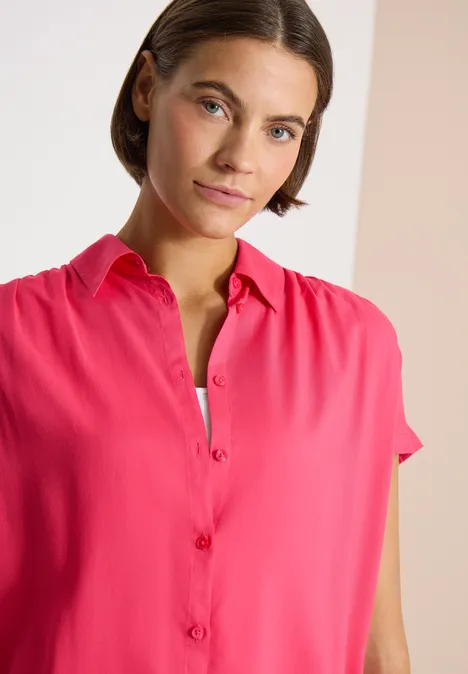 Een persoon met vaag gezicht draagt een felroze overhemd met korte mouwen en knoopsluiting.