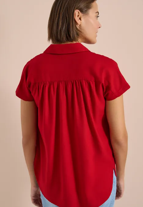 Frau von hinten in roter, kurzärmeliger Bluse mit gerafftem Rückenteil.