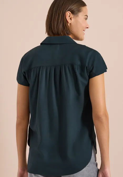 Eine Frau von hinten trägt eine kurze, dunkelgrüne Bluse mit kurzen Ärmeln.