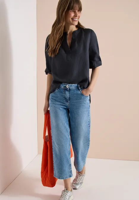 3/4-Arm Tunika aus reinem Leinen volcanic grey Frau trägt schwarze Bluse, weite Jeans, weiße Sneaker und eine orangefarbene Tasche vor neutralem Hintergrund.