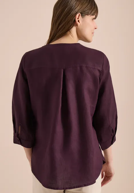 Vue de dos d’une femme portant un chemisier violet foncé à manches 3/4 et pli au dos.