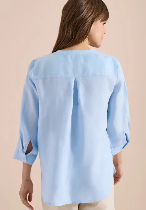 Rückenansicht einer Person in einer hellblauen, locker sitzenden Bluse mit Rückenzierfalte und 3/4-Ärmeln.