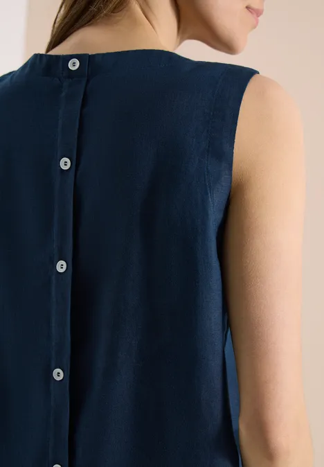 Eine Frau von hinten in einem ärmellosen, dunkelblauen Kleid mit durchgehender Knopfleiste am Rücken.