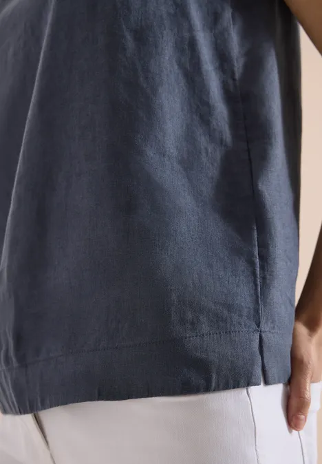 Nahaufnahme eines dunkelblauen Oberteils mit seitlichem Schlitz, kombiniert mit hellen Hosen und sichtbarer Hand.