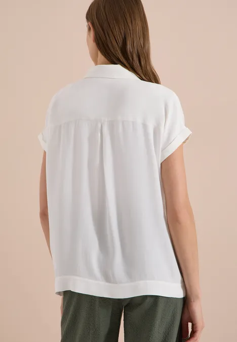 Kurzarm Hemdbluse in Unifarbe vanilla white Frau von hinten mit weißer kurzärmeliger Bluse und dunkelgrünen Hosen vor neutralem Hintergrund.