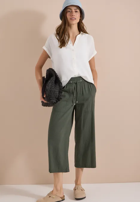 Kurzarm Hemdbluse in Unifarbe vanilla white Frau in weißer Bluse, olivgrüner Culotte, beigen Loafers und gewebter Tasche vor hellem Hintergrund.