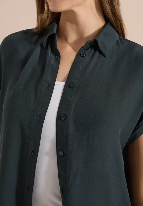 Kurzarm Hemdbluse in Unifarbe palm breeze green Eine Person trägt ein dunkles, kurzärmeliges Hemd über einem weißen Top.