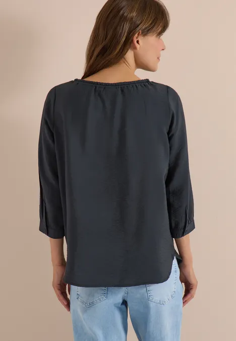 Chemisier Carmen à manches courtes et rubans palm breeze green Frau steht von hinten, trägt dunkelgraue 3/4-Ärmel-Bluse und helle Jeans.