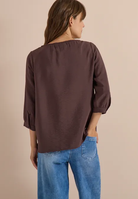Chemisier Carmen à manches courtes et rubans brown cacao Frau von hinten in brauner Bluse und blauer Jeans.