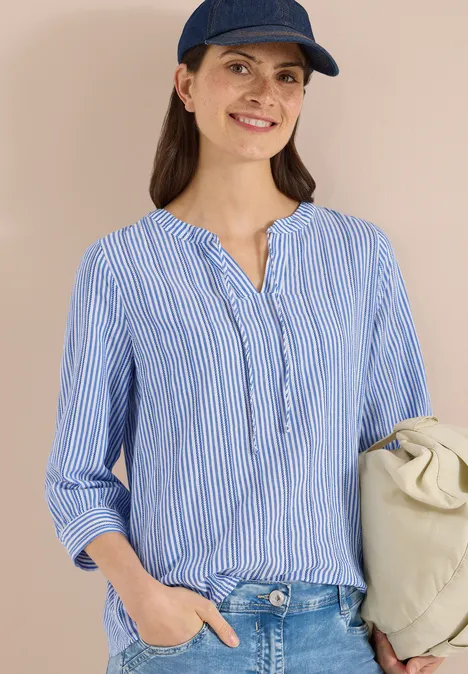 Persoon draagt blauw-wit gestreept blouse, jeans, blauwe pet en een lichte schoudertas.