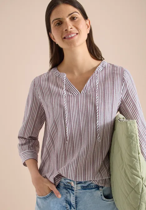 Gestreepte blouse met V-hals en driekwart mouwen, spijkerbroek en groene doorgestikte tas.