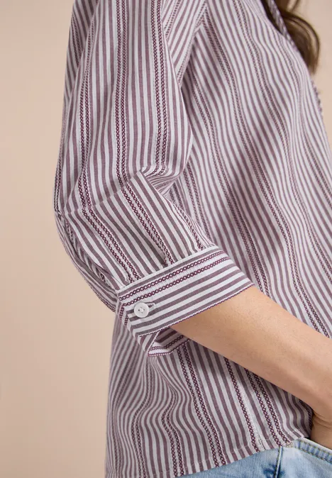 Close-up van een gestreept overhemd met opgerolde mouw, gecombineerd met een spijkerbroek.