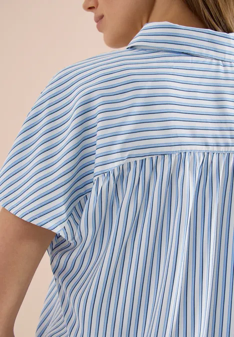 Achteraanzicht van een vrouw in een lichte, kort mouw blouse met blauw-witte verticale strepen.