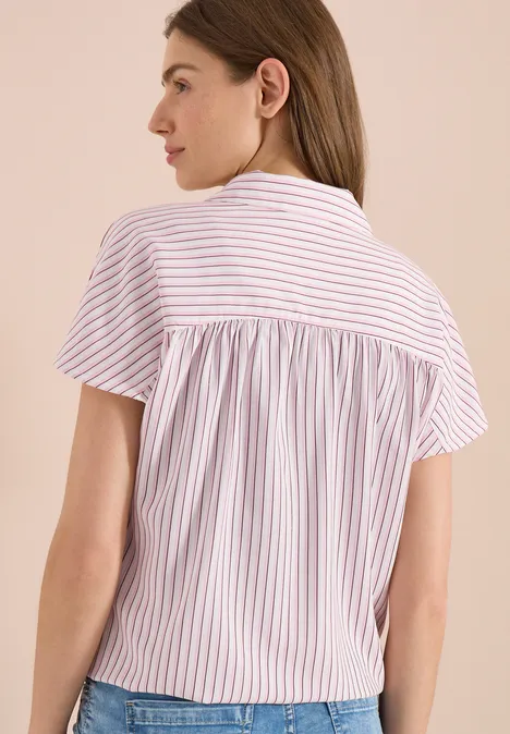 Achteraanzicht van een vrouw in een losse, kortmouwige blouse met roze-witte strepen.