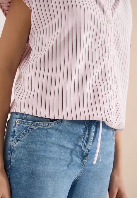 Een persoon draagt een roze-wit gestreept bloesje en blauwe spijkerbroek.