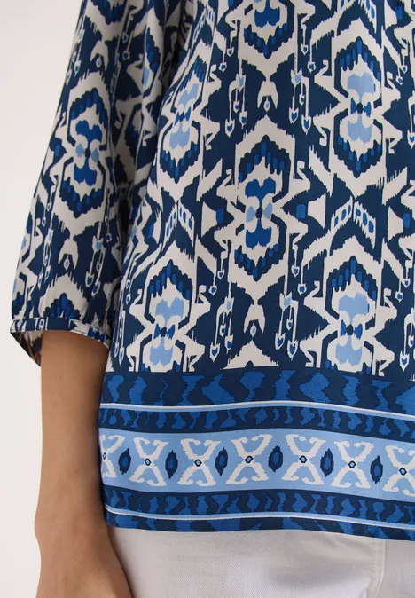 Vrouw draagt blauw-wit dessin top met driekwart mouwen en sierlijke zoom