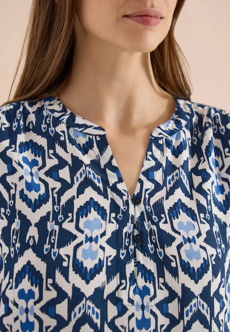 Een vrouw draagt een blauw-witte blouse met geometrisch patroon.