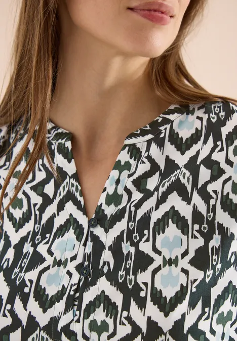 Close-up: vrouw in blouse met zwart-wit-groen ikatpatroon en subtiele V-hals.