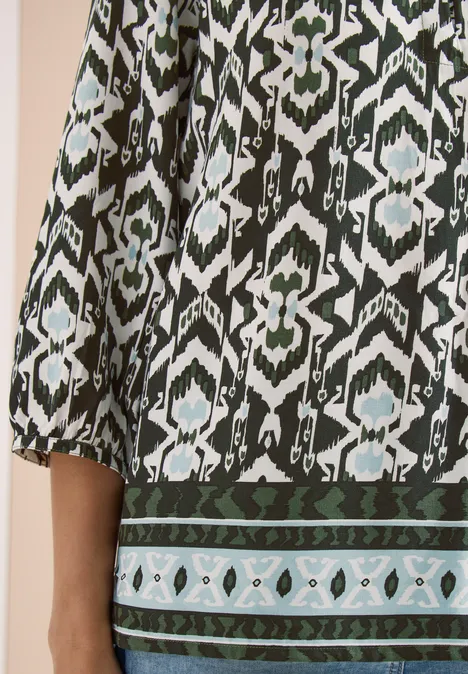 Close-up van een groen-zwart-wit etnisch dessin op een kledingstuk met lange mouwen.