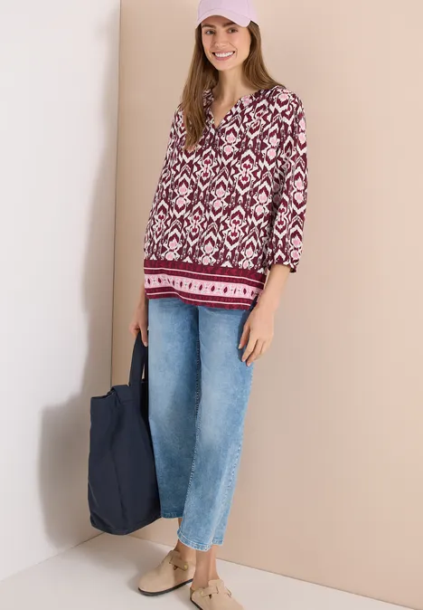 Vrouw draagt gebloesd topje met V-hals, wijde spijkerbroek, beige schoenen en een blauwe stoffen tas.