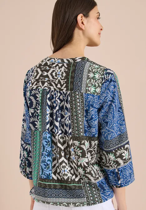 Vrouw van achteren in een patchworkblouse met 3/4-mouwen en bloemenprint in blauw, groen en zwart-wit.
