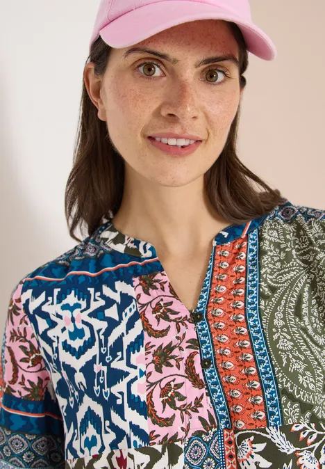 Vrouw met roze pet en kleurrijke patchworkblouse, gezicht onscherp.